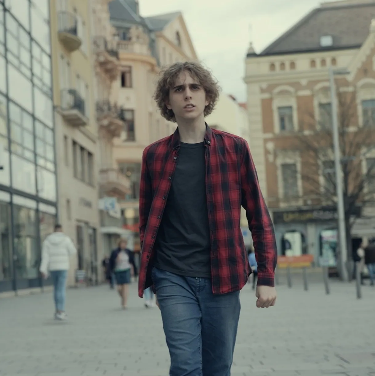 A photograph of Misha walking down a town square while staring up into the distance.
